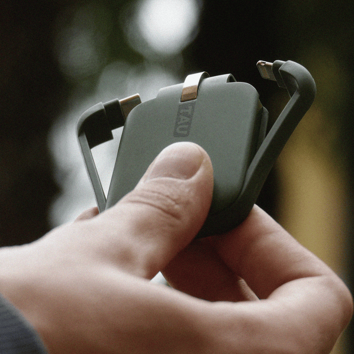 TAU® - Always-charged power bank - Charcoal Black - Compact agave green TAU power bank with built-in charging cables held in hand outdoors. - Rolling Square